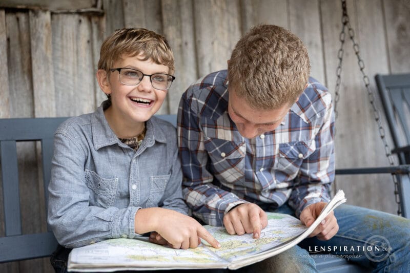 Two boys look at an atlas together on a swing on a porch
