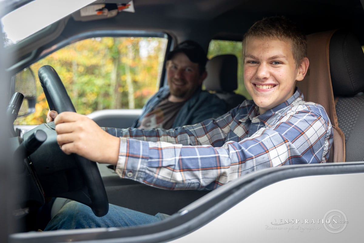 Father and son smile at the camera while learning how to drive. Drivers education.