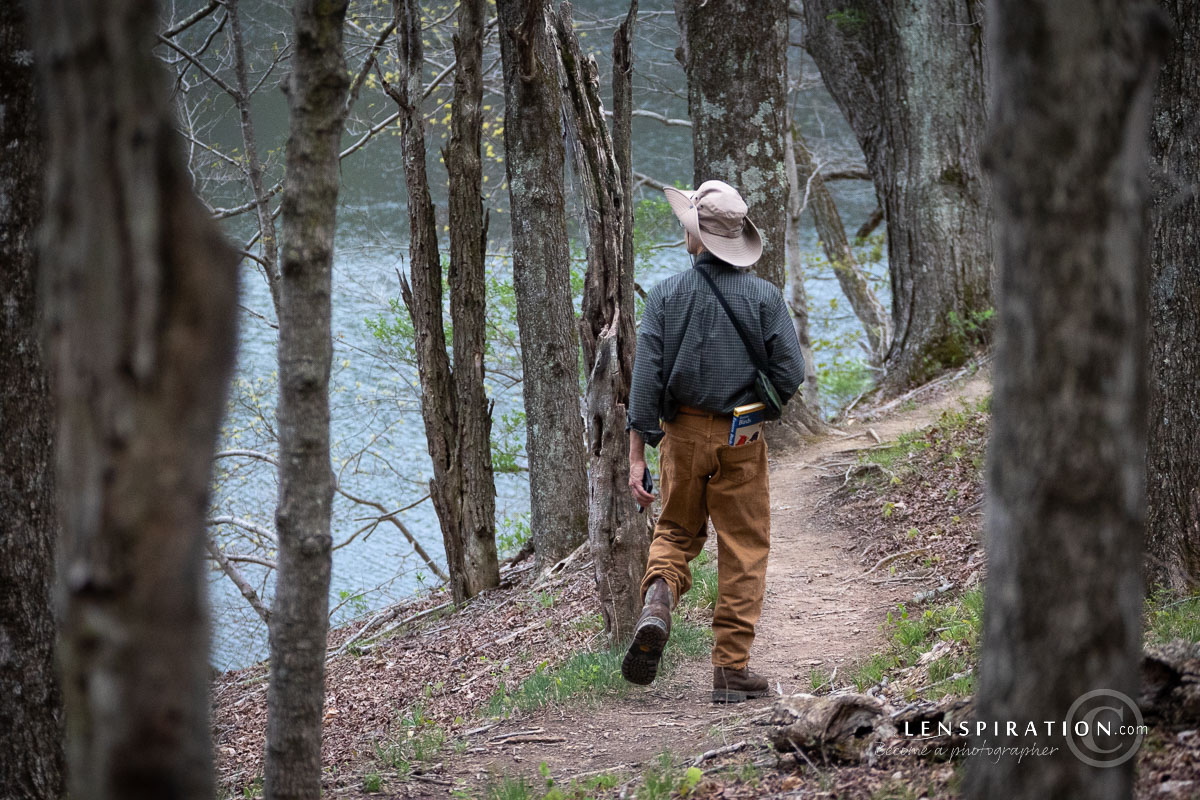 A birdwatcher hikes through the forest by a lake looking for birds